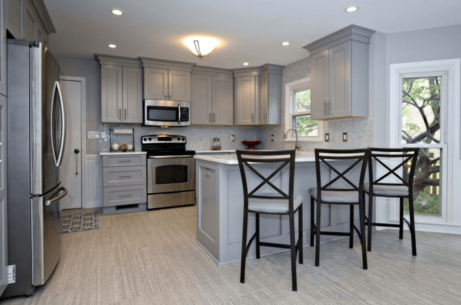 Large kitchen with light grey cabinets and breakfast bar with white countertop.